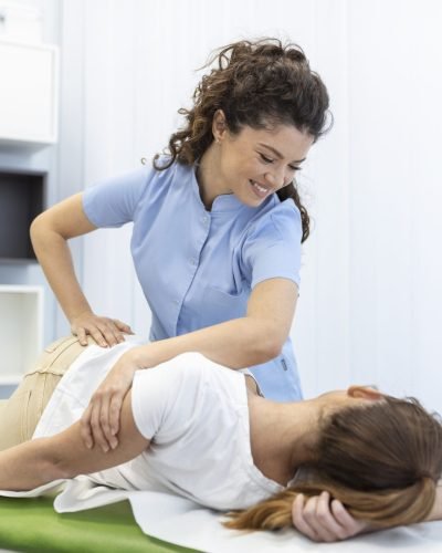 Young woman doctor chiropractor or osteopath fixing lying womans back with hands movements during visit in manual therapy clinic. Professional chiropractor during work